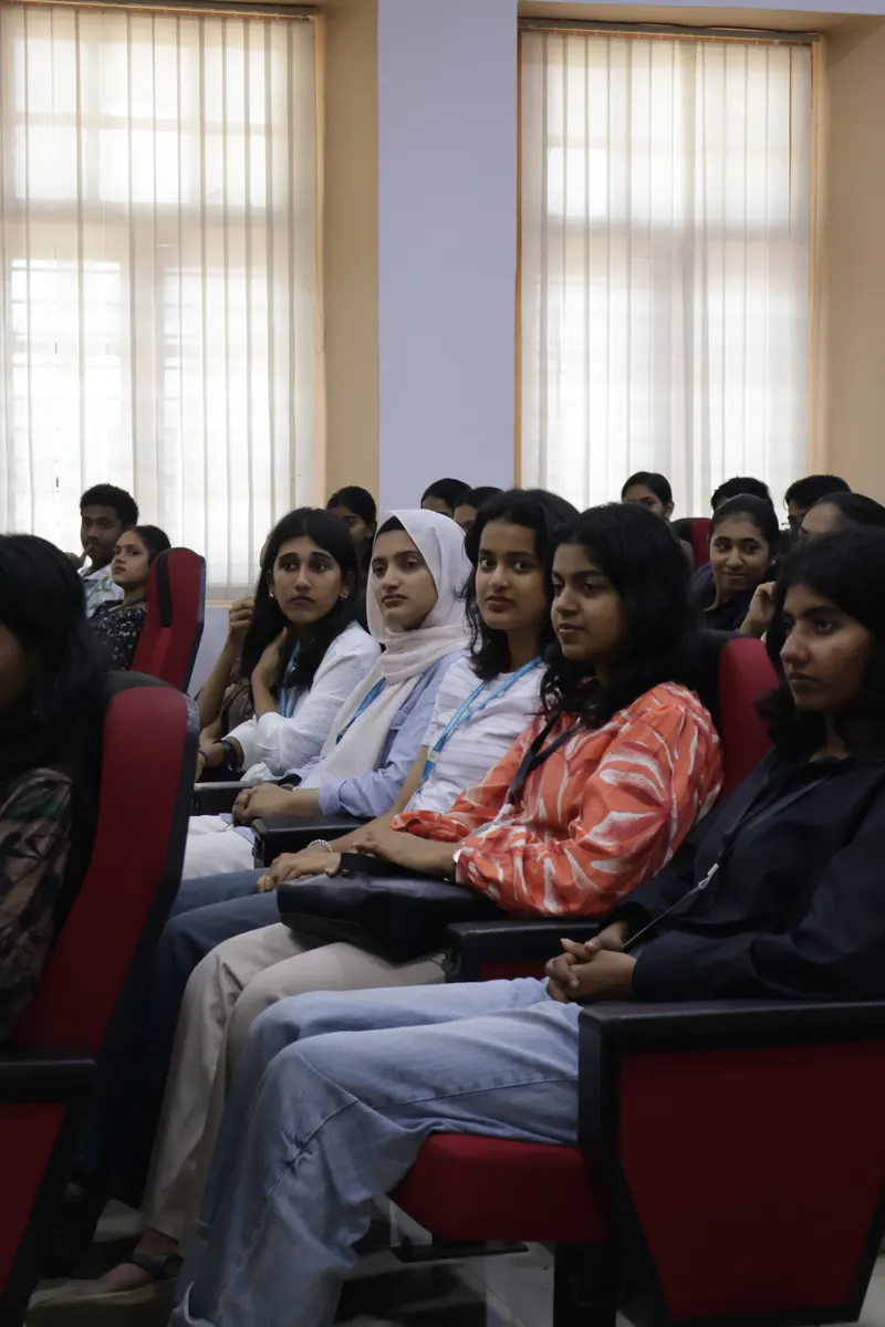 Students seated in the auditorium beside the tall windows, watching the stage