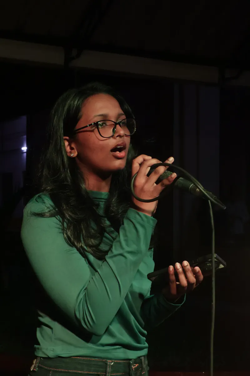 A student performing a song, microphone in hand, on a darkened stage