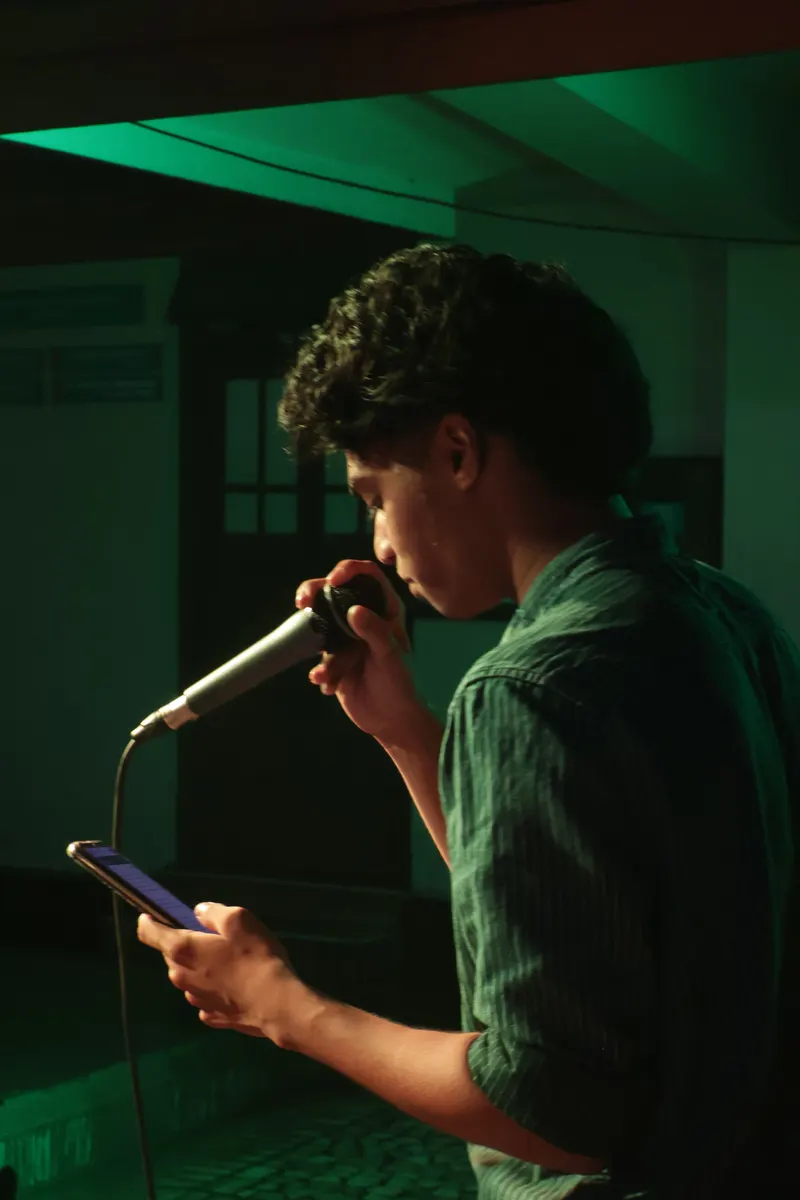 A performer lit in green stage light, reading lyrics from a phone