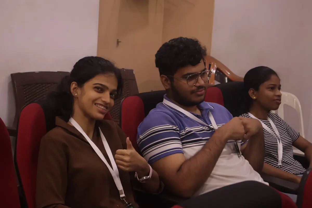 Three students in the audience, one giving a thumbs up to the camera