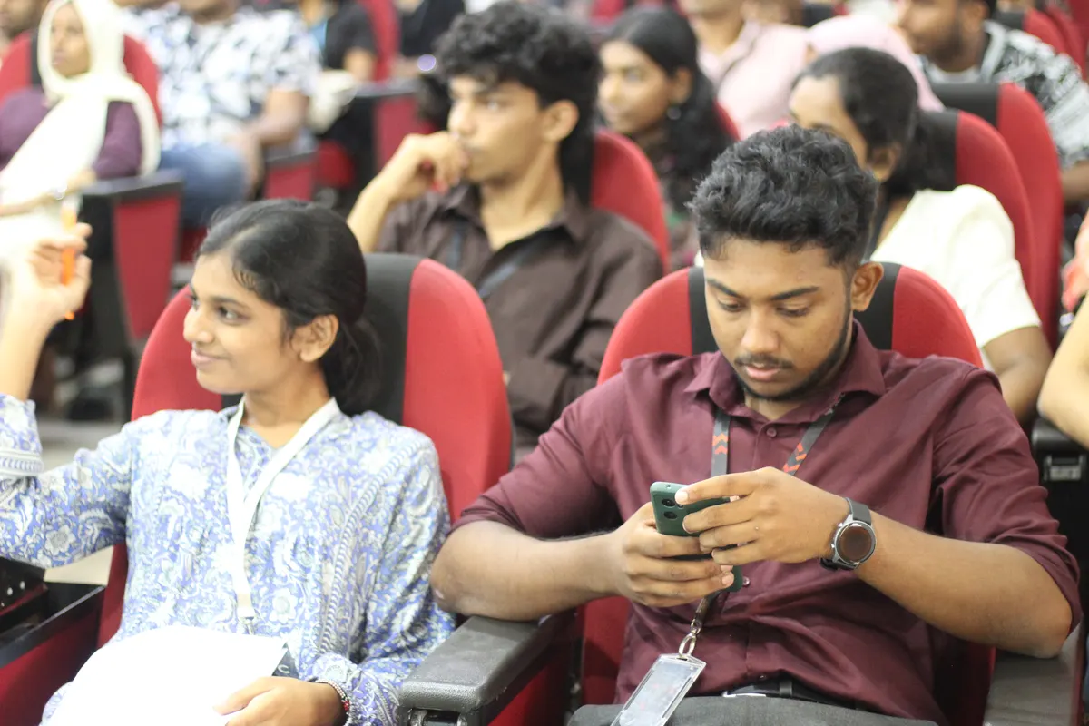 Two students seated side by side, one looking at a phone