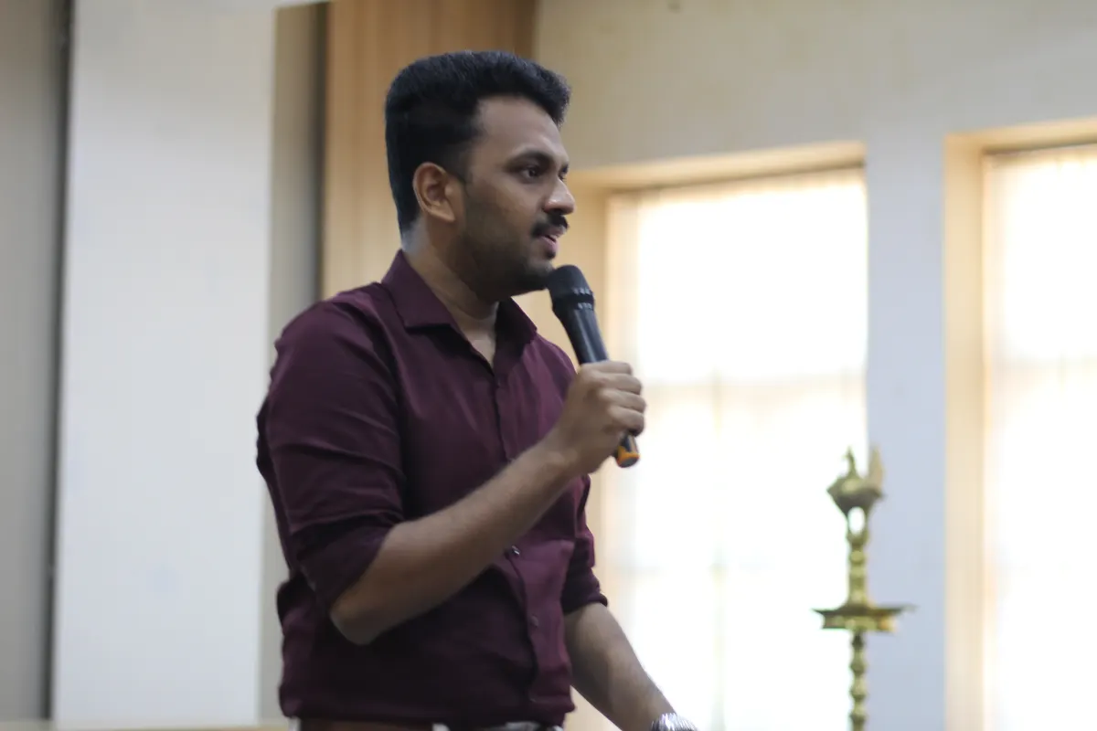 A speaker addressing the room with a microphone, ceremonial lamp beside them